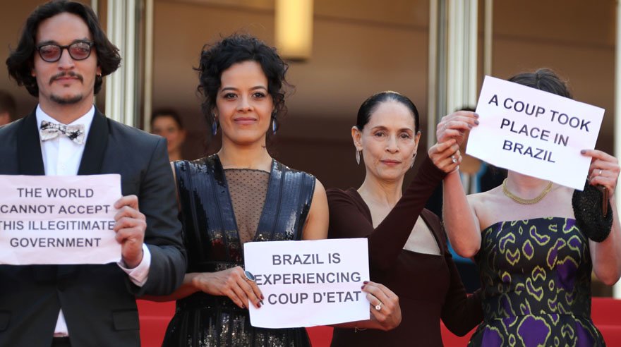 (FromL) Brazilian actor Allan Souza, Brazilian actress Maeve Jinkings, Brazilian actress Sonia Braga and French-Brazilian producer Emilie Lesclaux hold protest signs as they arrive on May 17, 2016 for the screening of the film "Aquarius" at the 69th Cannes Film Festival in Cannes, southern France. / AFP / Valery HACHE